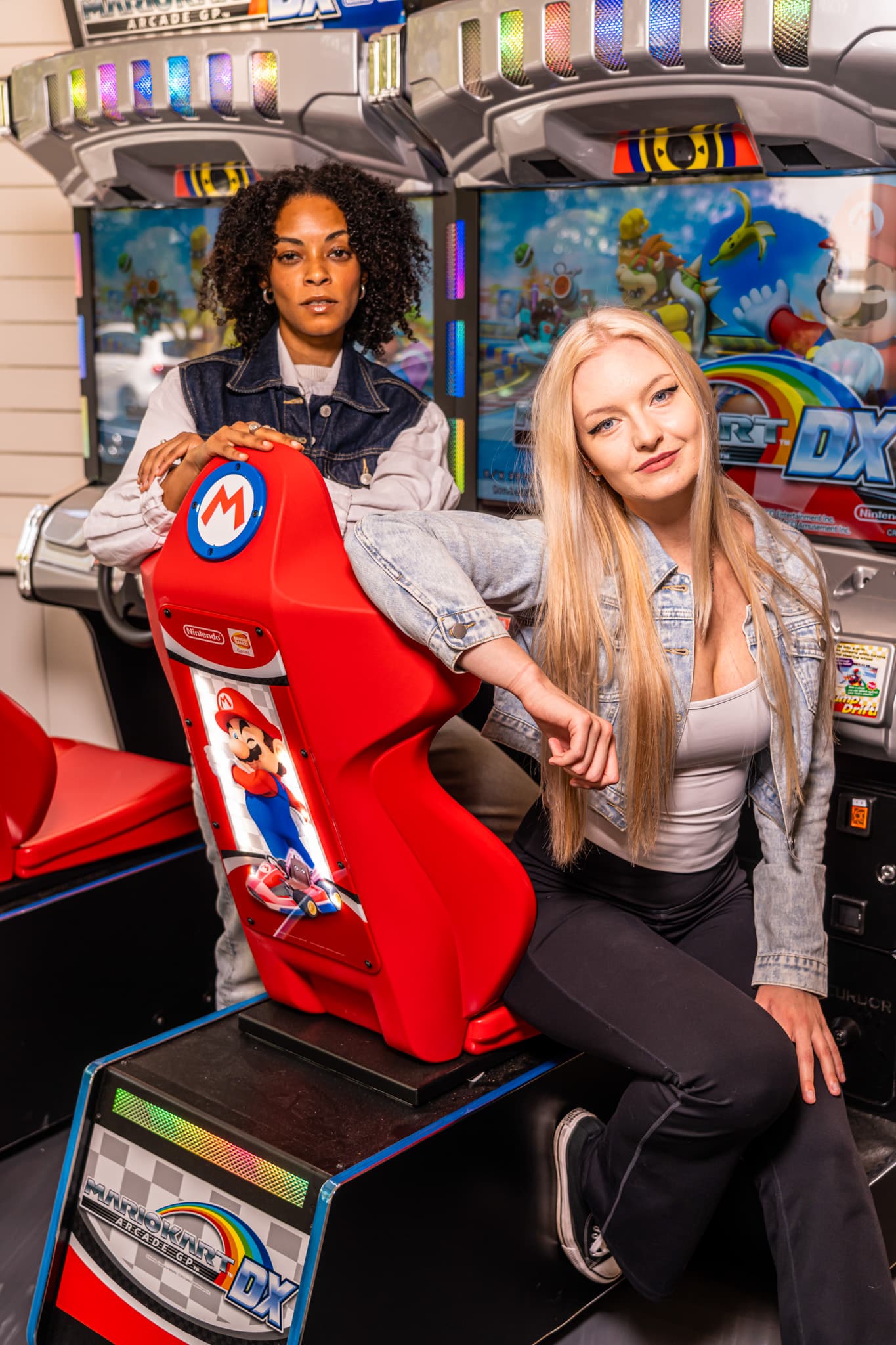 Two friends posing together at a Mario Kart racing cabinet