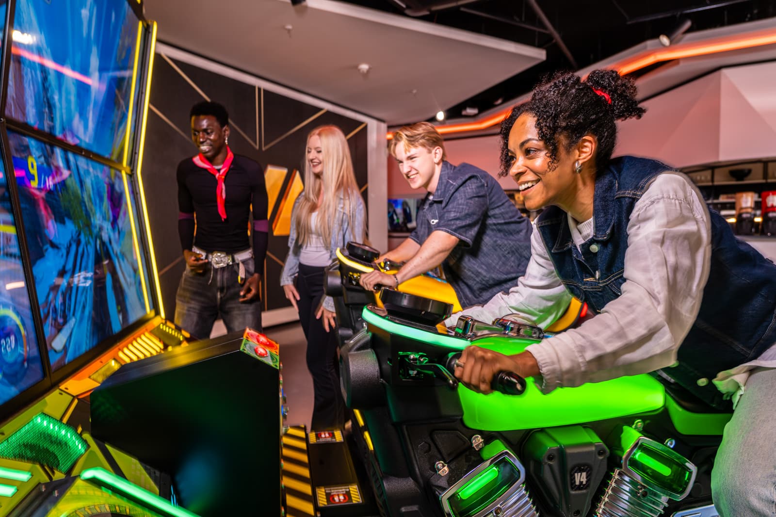 A group of friends laughing together while racing on arcade motorbike cabinets